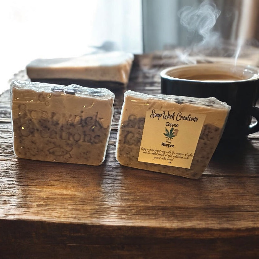 Two bars of coffee scented soap sitting on a wooden table with a steaming hot cup of coffee.