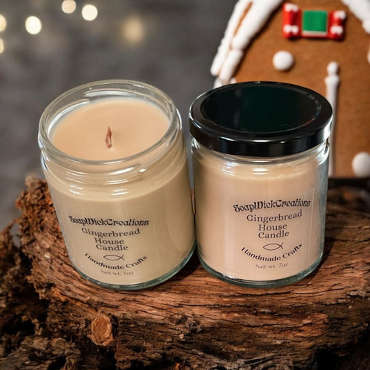 Two tan colored gingerbread candles with wooden wicks, sitting on a log with a gingerbread house in the background.