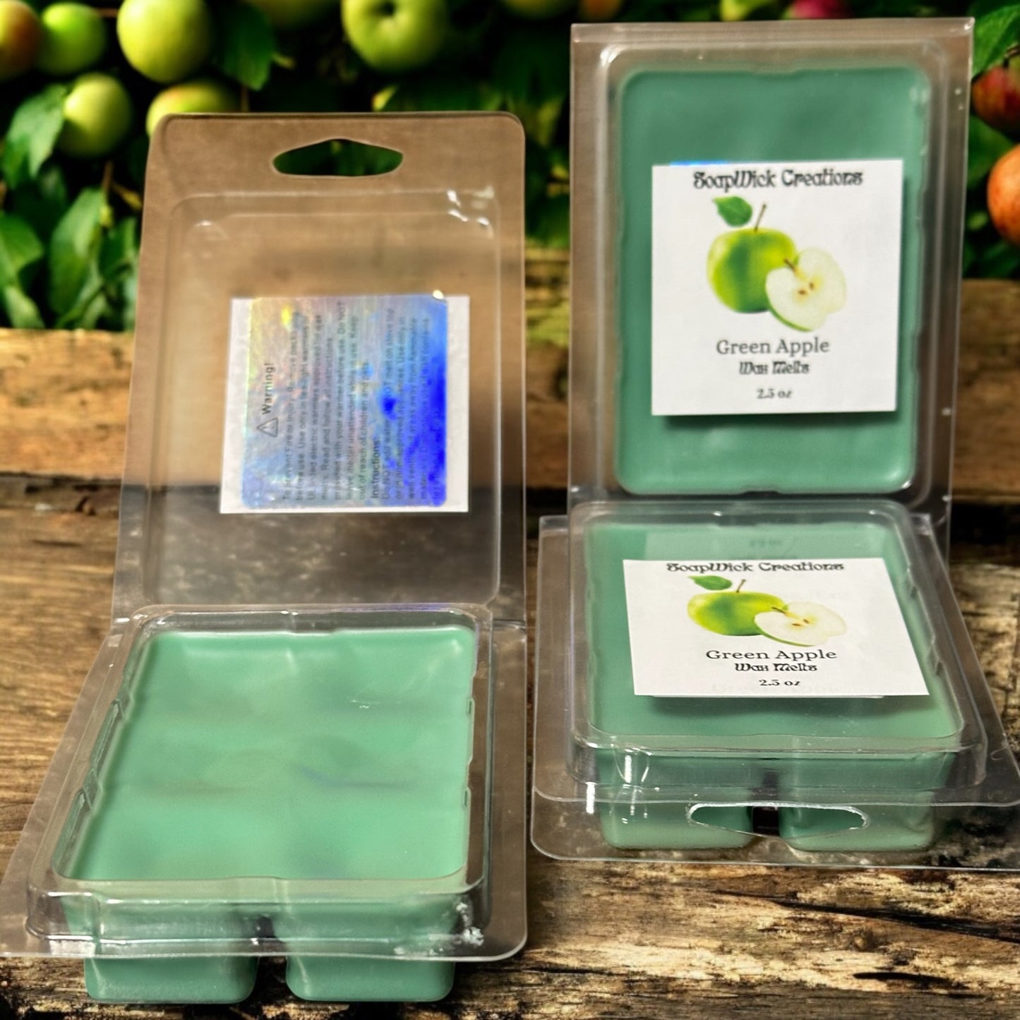 3 Green Apple scented wax melts in plastic containers sitting on a wooden bench with apple trees with apples in the background