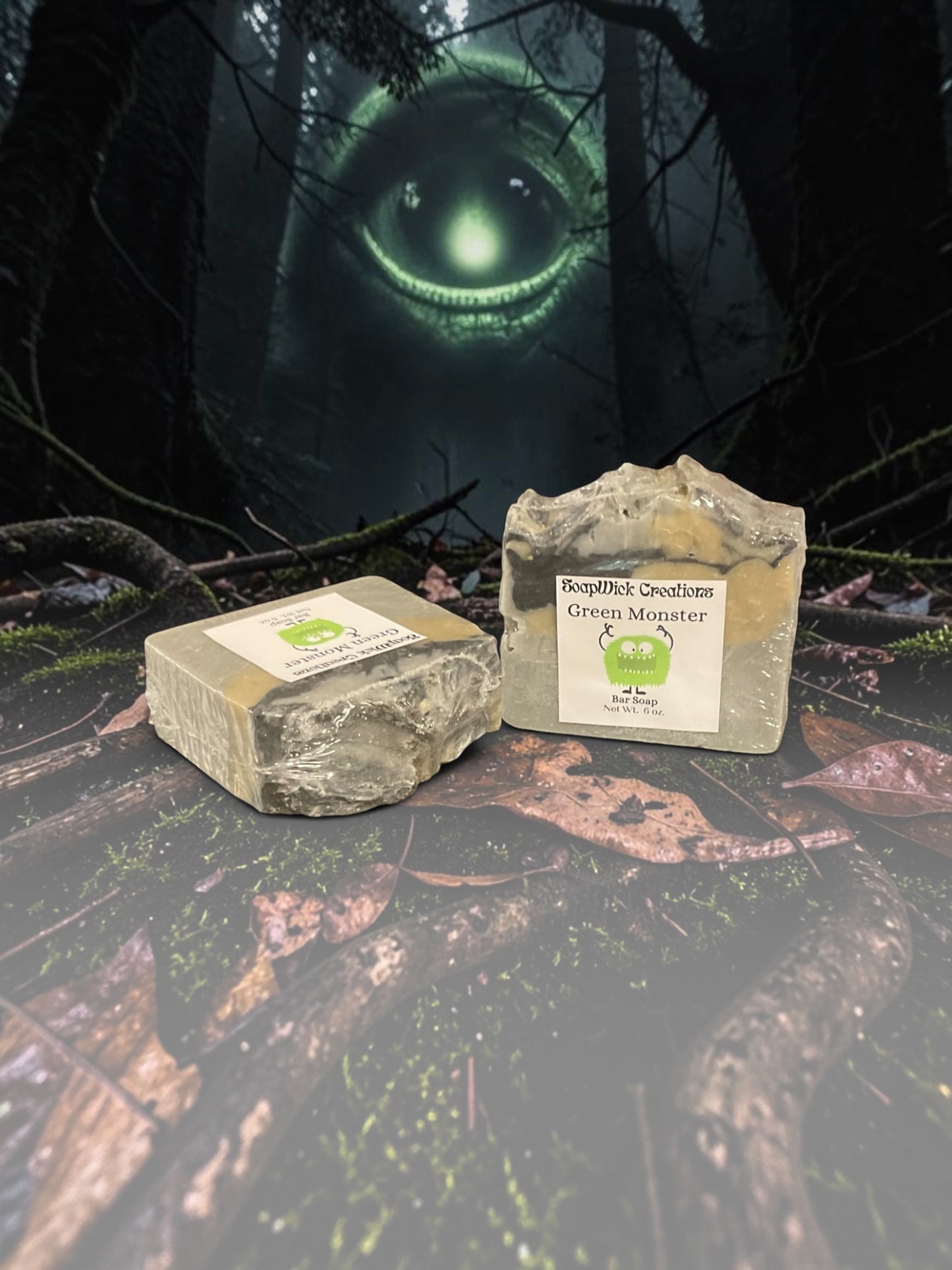 Two bars of beige, black and gold, Green Monster soap sitting on a log in the middle of a forest with a large green monster in the background.