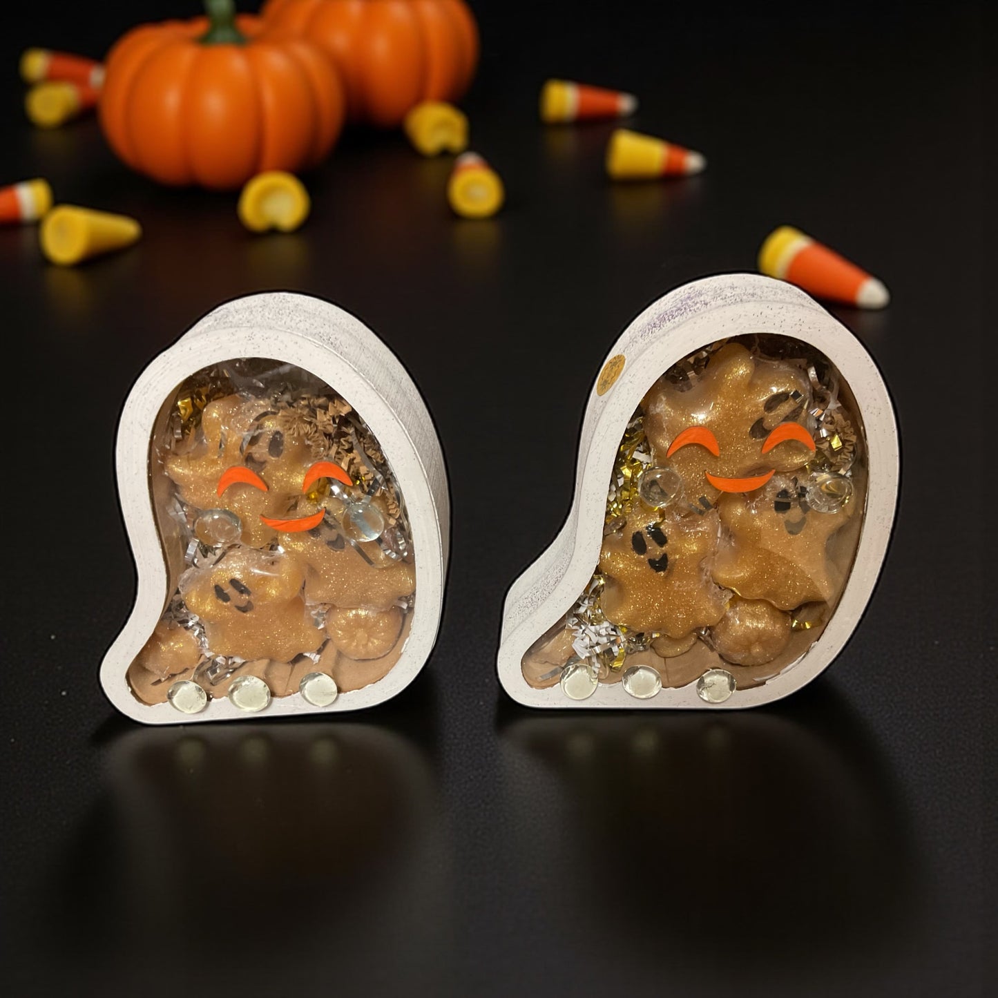 Hand painted and decorated ghost shaped wooden boxes containing glycerin poured soaps with vampire blood scent. In the background is candy corn and pumpkins all sitting on a table top.