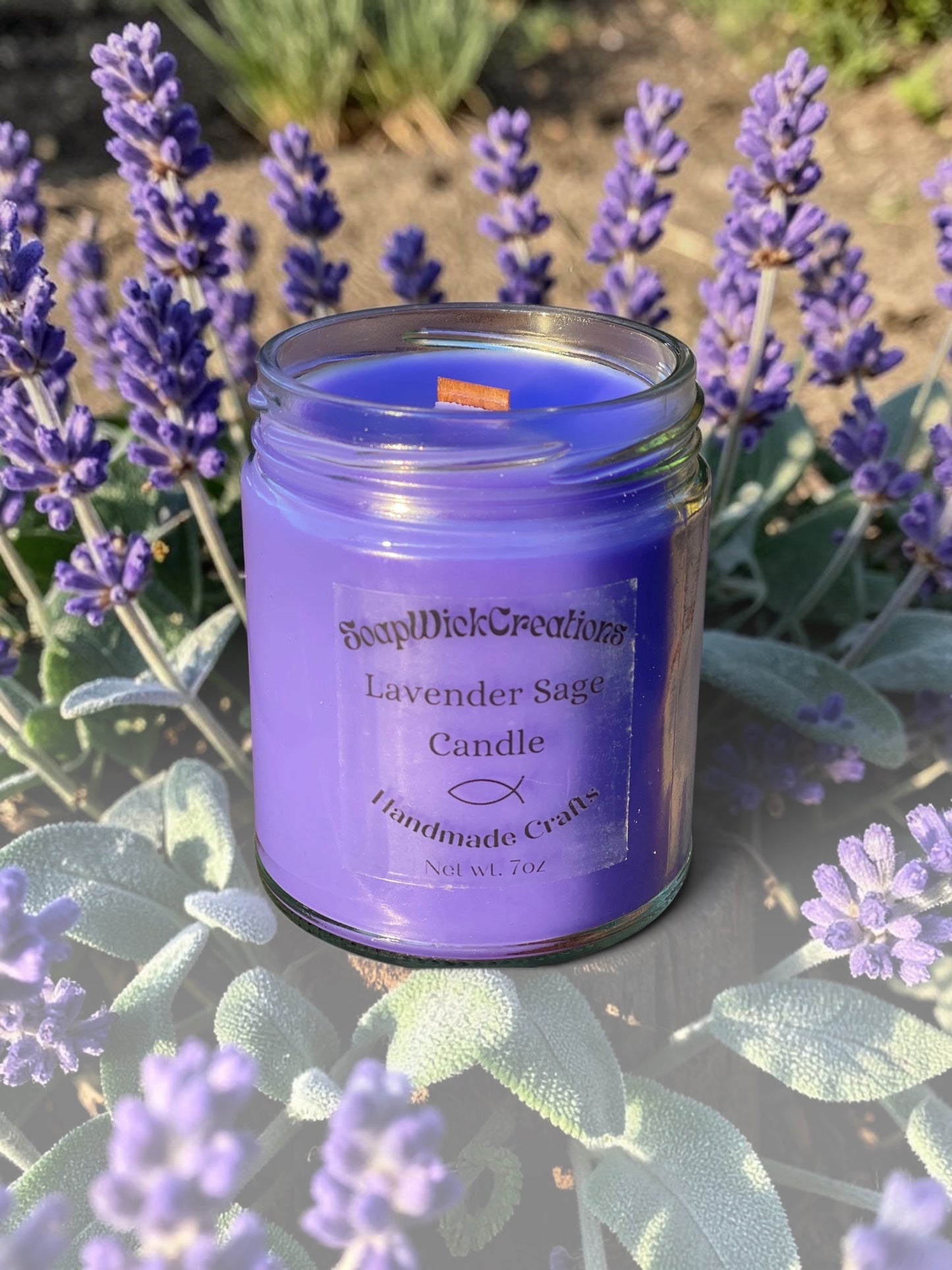 Lavender Sage scented candle in a clear glass jar with a purple wax fill and a wooden wick, set outdoors among blooming lavender flowers.