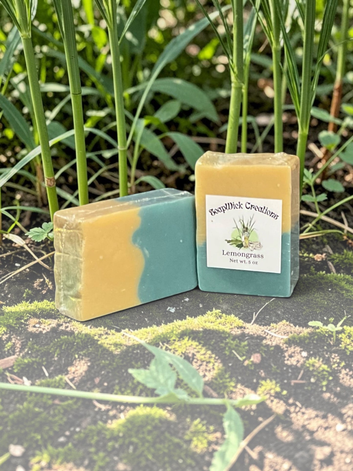 Two Beijing green colored bar soaps, sitting in a field with lemon grass surrounding them