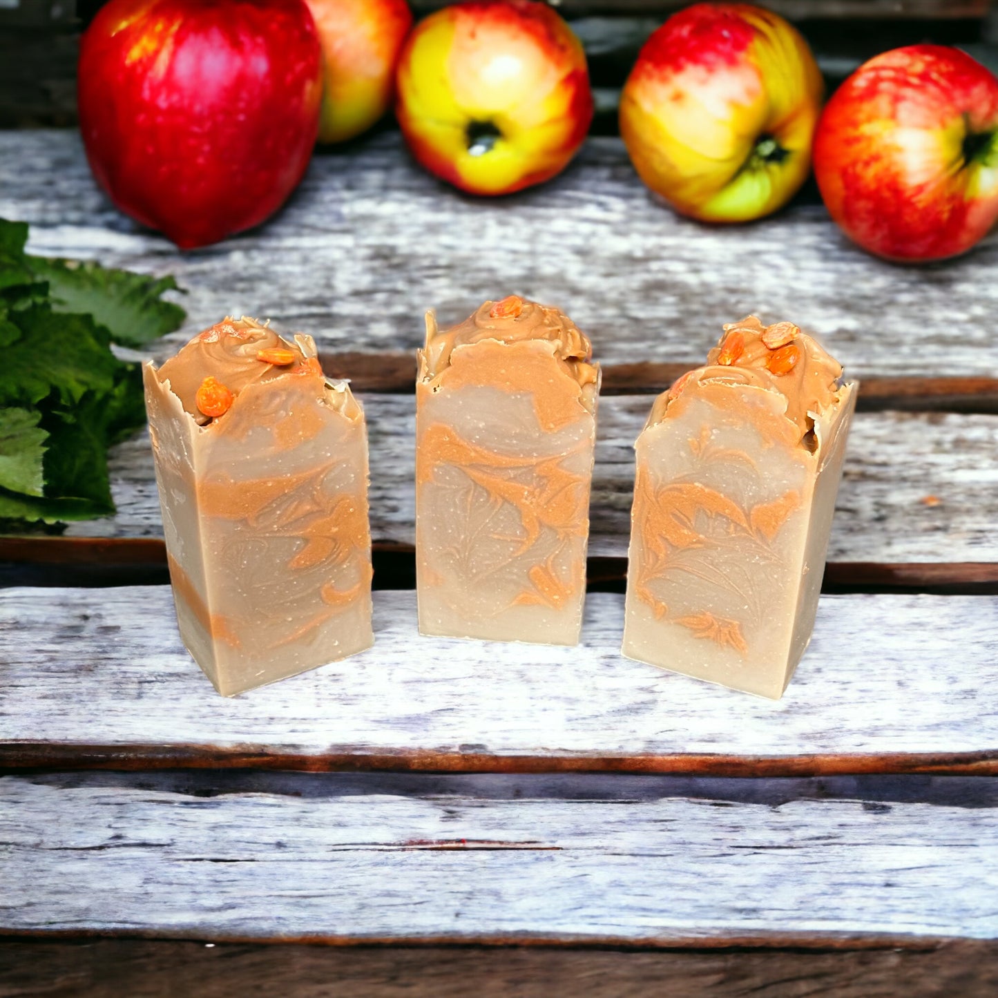 3 orange and beige colored bars of soap with Dunkin' Apple scent on a rustic white bench with apples in the background.