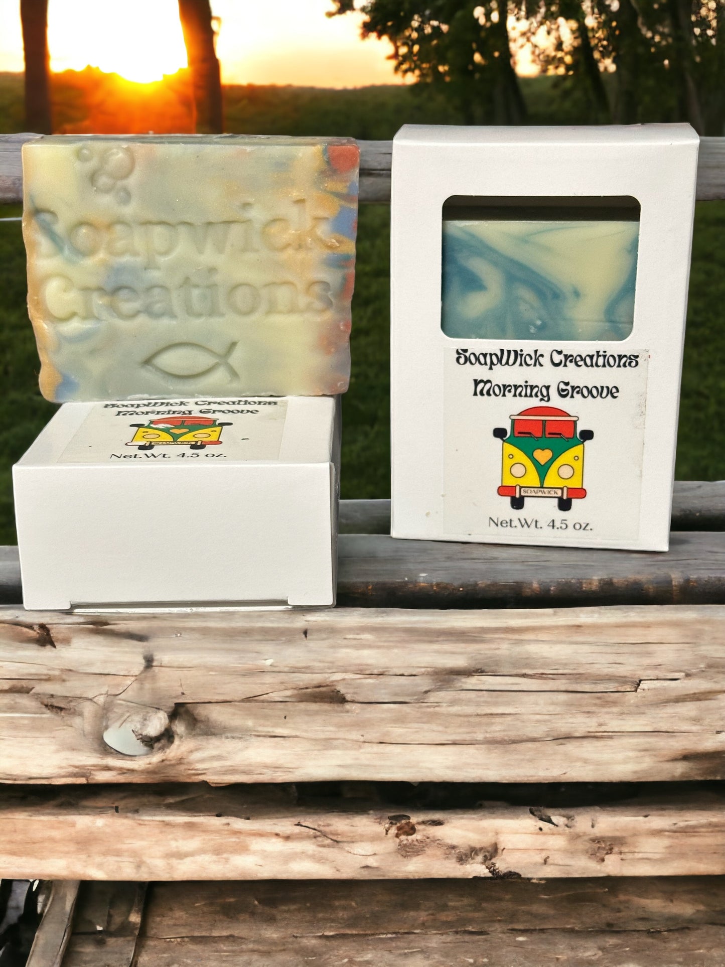 Two multi-colored soap bars with a fresh morning scent on a rustic bench with a sunrise in the background.