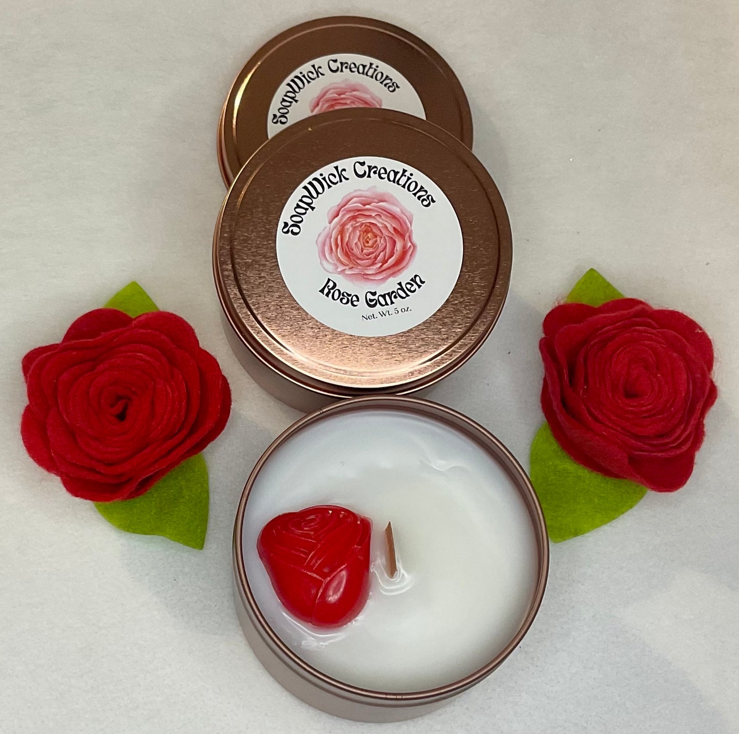Photograph of rose, colored tins with white rose, scented candle and red rose embed.