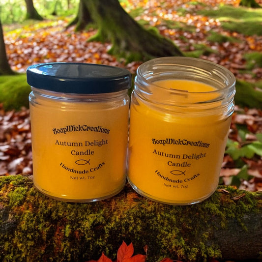 Two autumn delight, orange, colored, scented candles, sitting on a fallen log in a forest during the fall with leaves and trees in the background