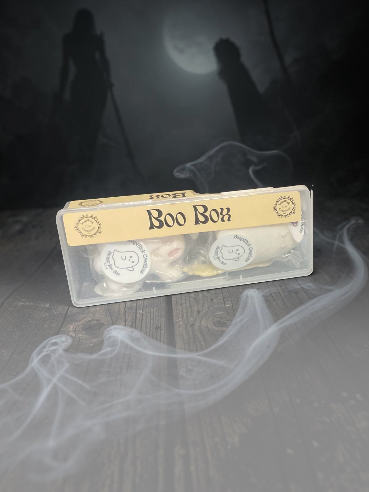 A clear plastic box labeled 'Boo Box' containing small Pumpkin Spice Shampoo Bars placed on a dark wooden surface with smoky white effects and a spooky moonlit background.