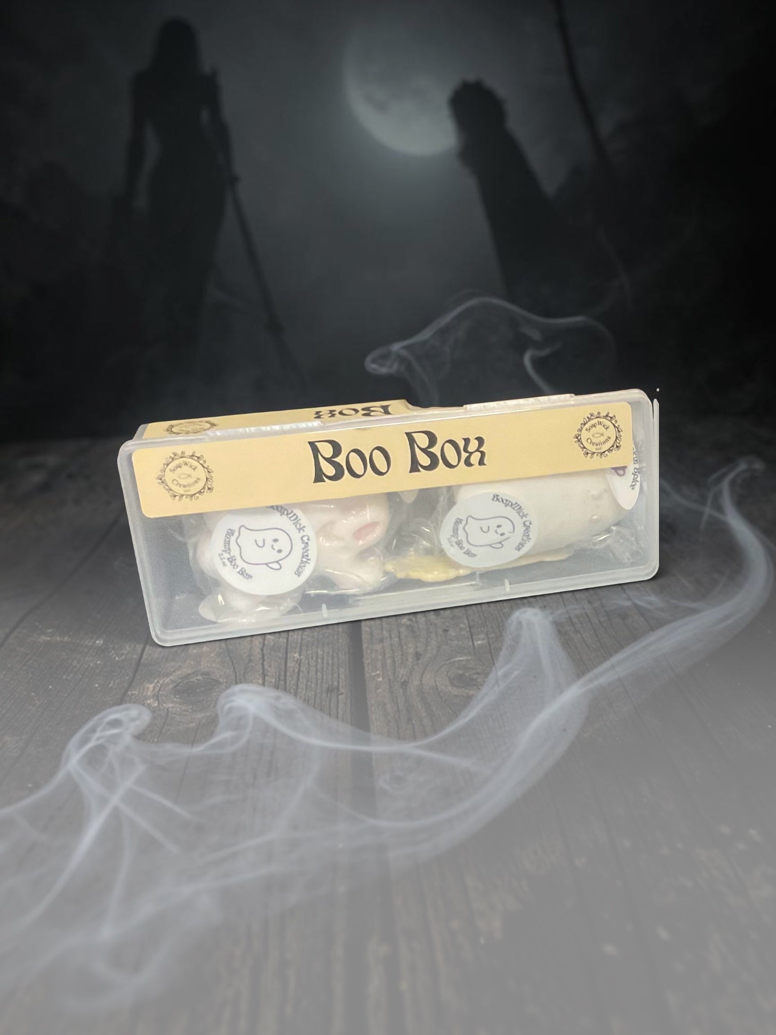 A clear plastic box labeled 'Boo Box' containing small Pumpkin Spice Shampoo Bars placed on a dark wooden surface with smoky white effects and a spooky moonlit background.