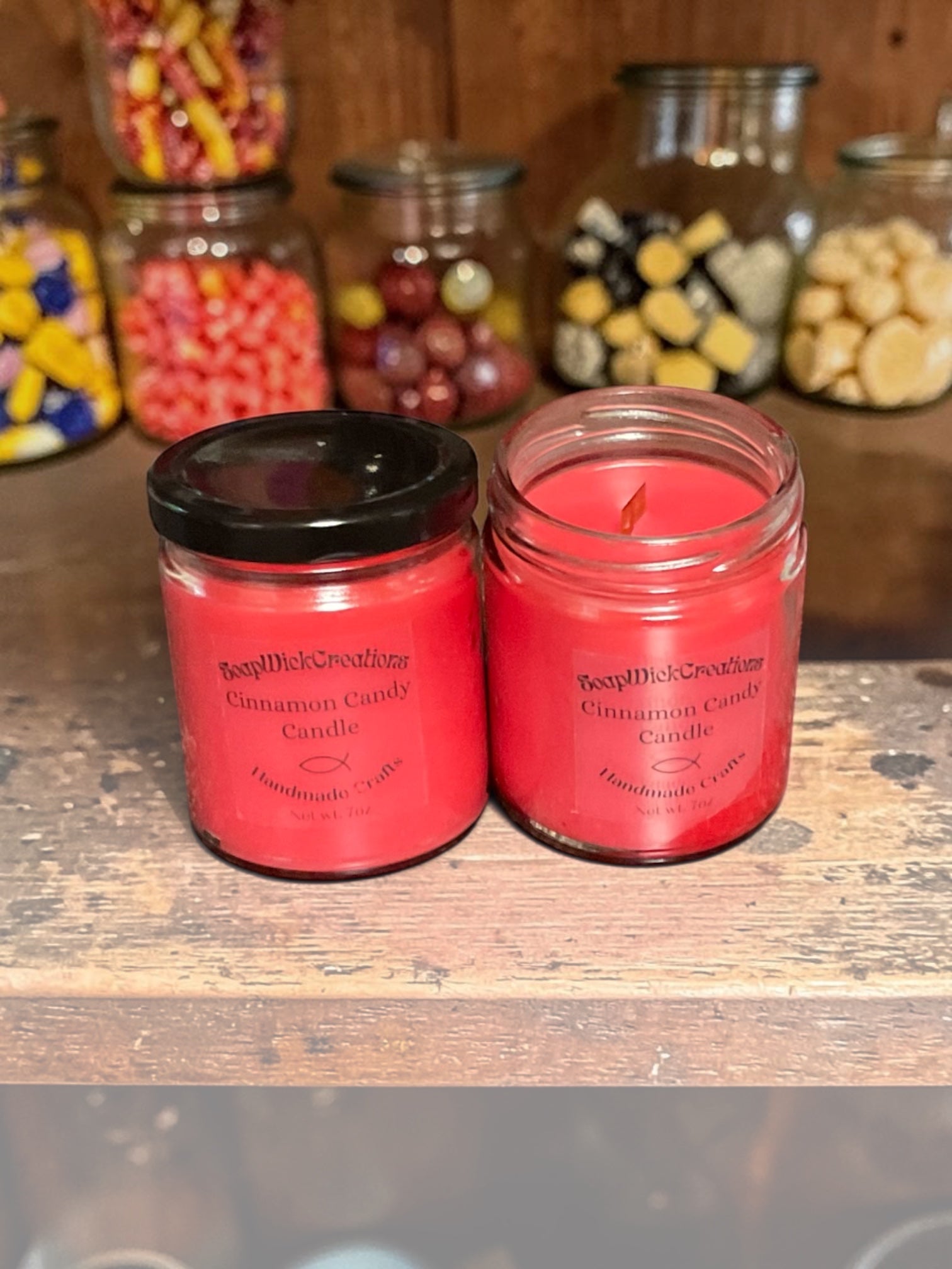 Two red cinnamon candies, jar, candles, sitting on a shelf surrounded by candy jars full of candy in a candy shop.