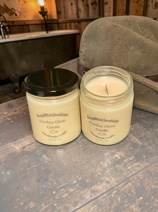 Two beige colored cowboy clean scented candles, sitting on a table next to a cowboy hat with a bathtub  in the background in an 1860 style hotel room.