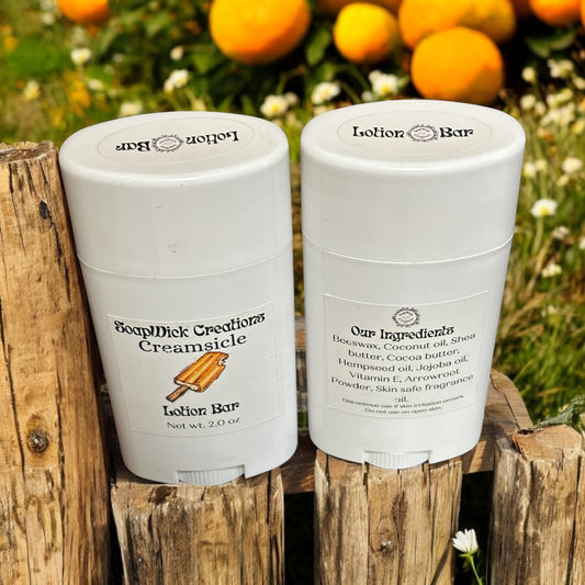 Two white tubes containing Creamsicle lotion bars sitting on a fence post with oranges in a  pasture in the background.