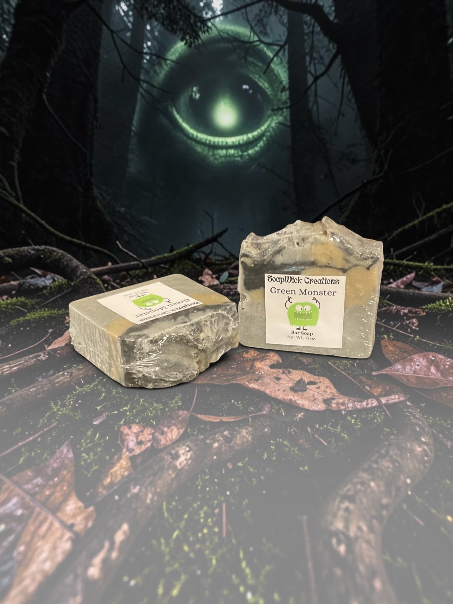 Two bars of beige, black and gold, Green Monster soap sitting on a log in the middle of a forest with a large green monster in the background.