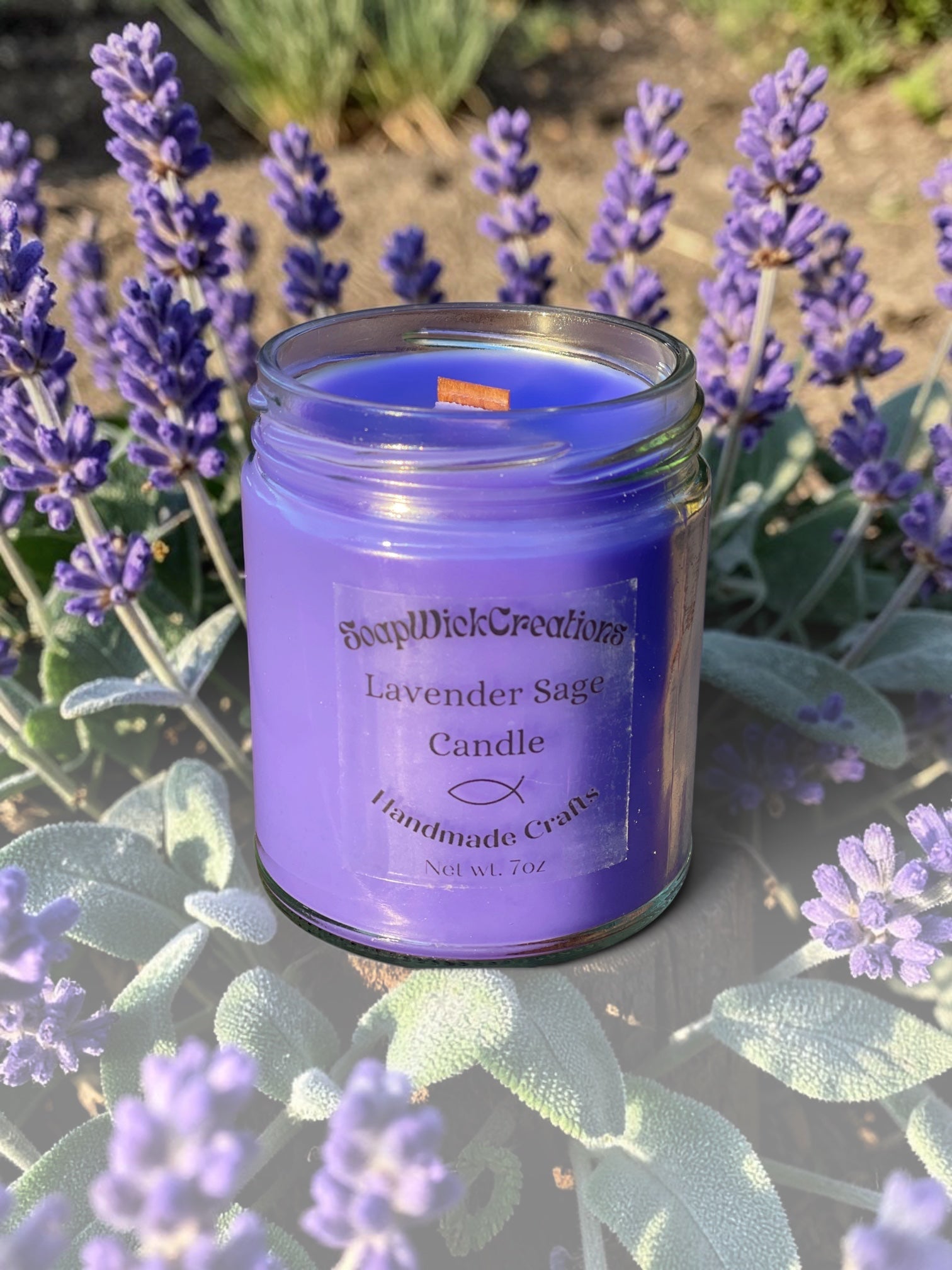 Lavender Sage scented candle in a clear glass jar with a purple wax fill and a wooden wick, set outdoors among blooming lavender flowers.