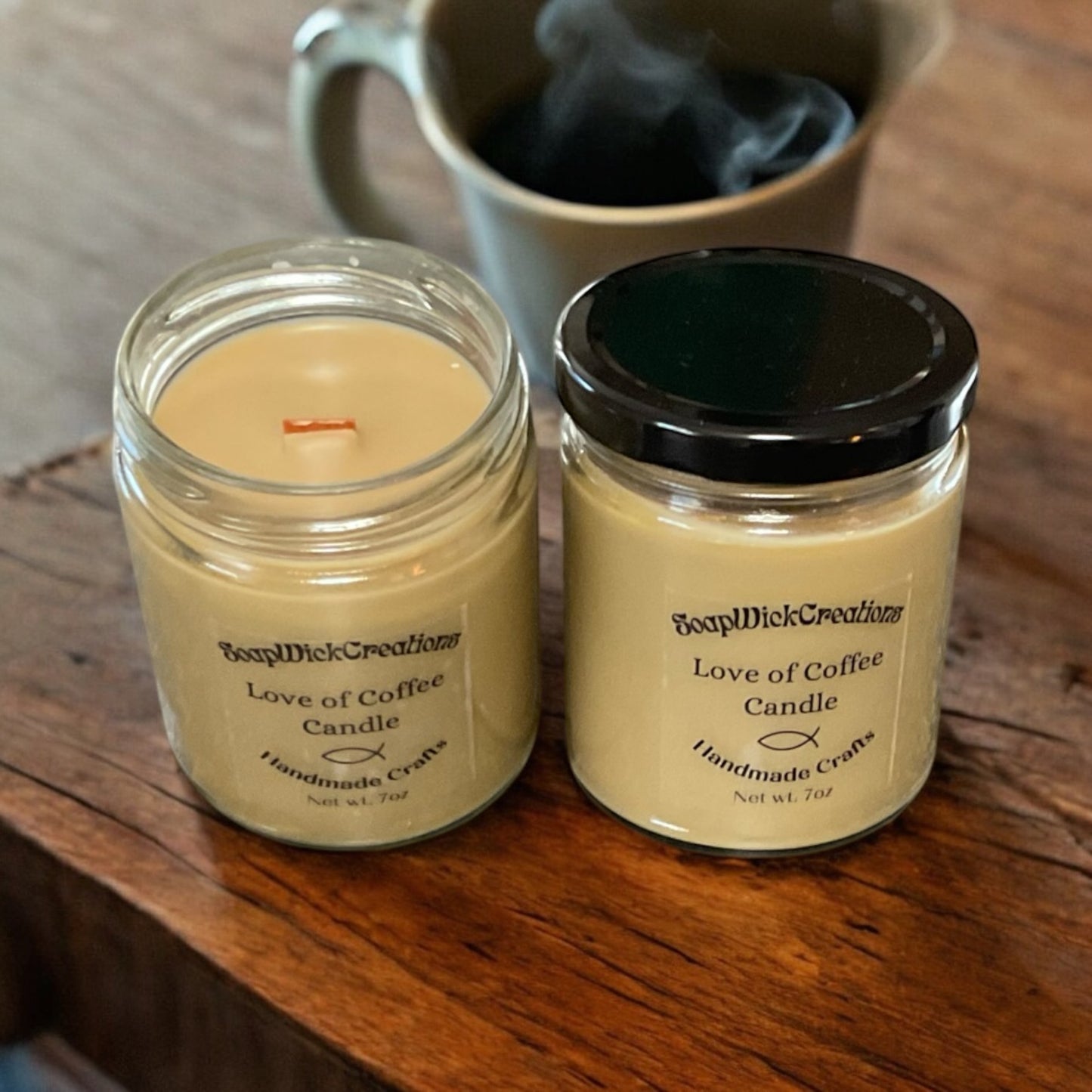 Two light brown candles in jars with the aroma of freshly roasted coffee, sitting on a table with a steaming cup of coffee in the background.