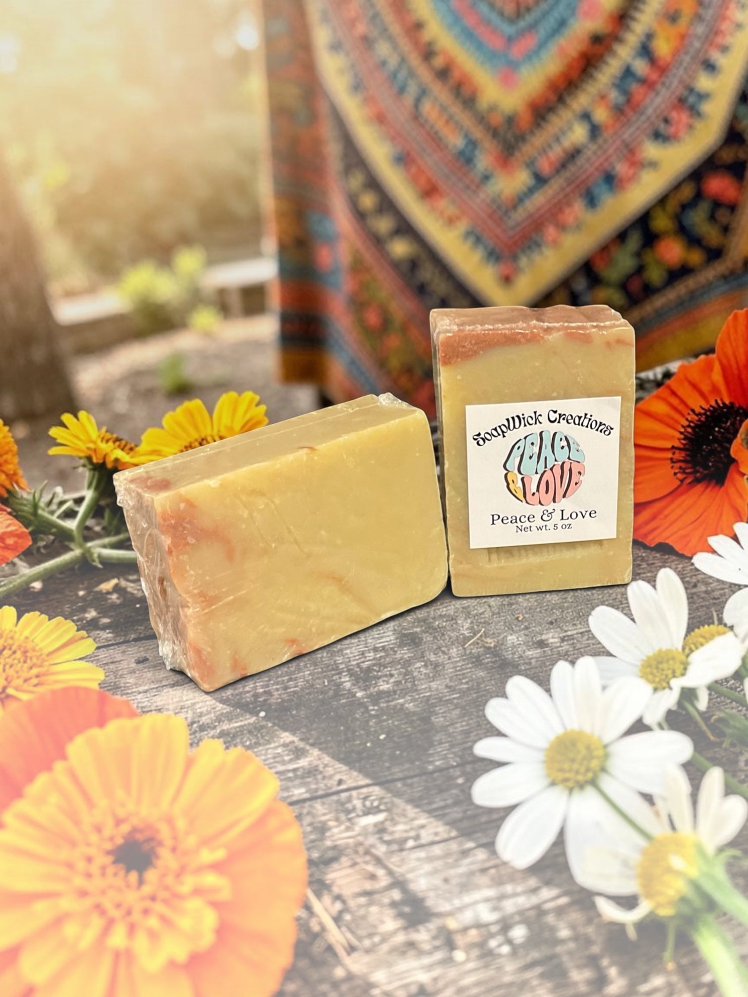 Two Peace and Love bar soap sitting on a wooden table in an old garden shed, surrounded by colorful flowers, and a colorful backdrop with a window in the background.