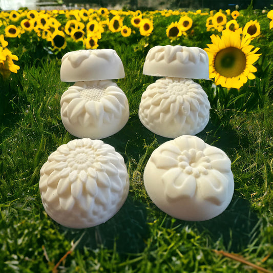 White flower molded shampoo bars on a patch of grass with a sunflower field in the background.