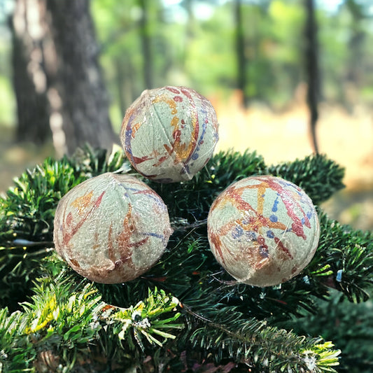 Forest Pine scented bath bombs on a pine bough with pine trees in the background.