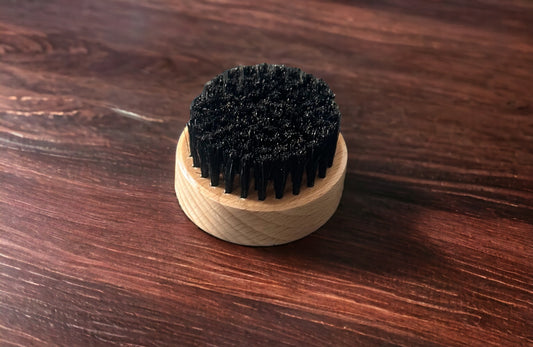 A round 2 inch beard brush with natural bore bristles sitting on a wooden table.
