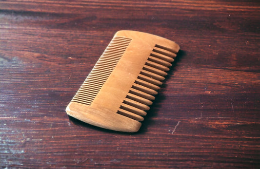 Approximate 3 inch beard comb sitting on a dark wooden table.