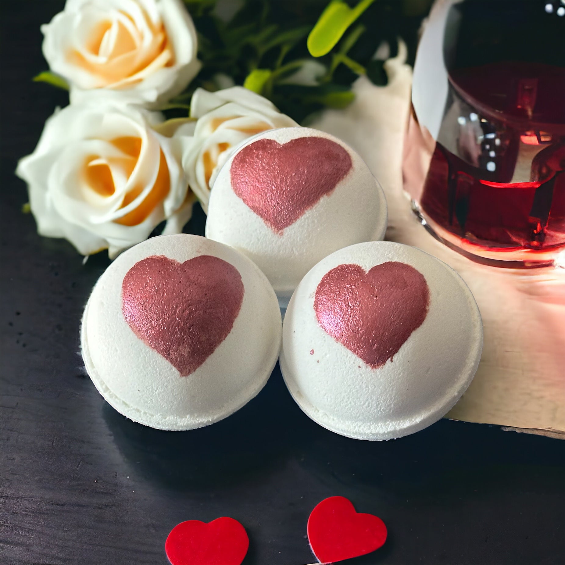 Three hand painted romantic interlude bath bombs with roses, wine and hearts in the background.