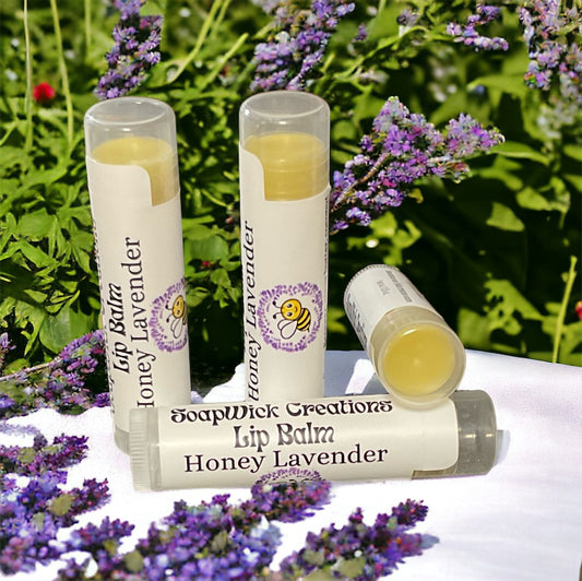 Three tubes of honey, lavender, flavored lip balm, sitting on top of a beehive with a field of lavender flowers around it.