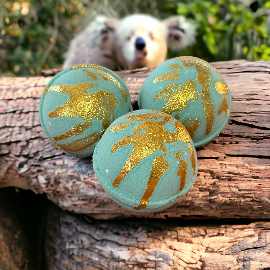 Photograph of Eucalyptus Mint scented light green round bath bombs with gold glitter sitting on a log with a koala bear in the background.