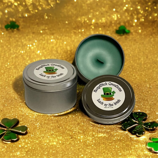 Two Luck of the Irish green candles with wooden wicks in silver tins on a gold background with shamrocks around them.