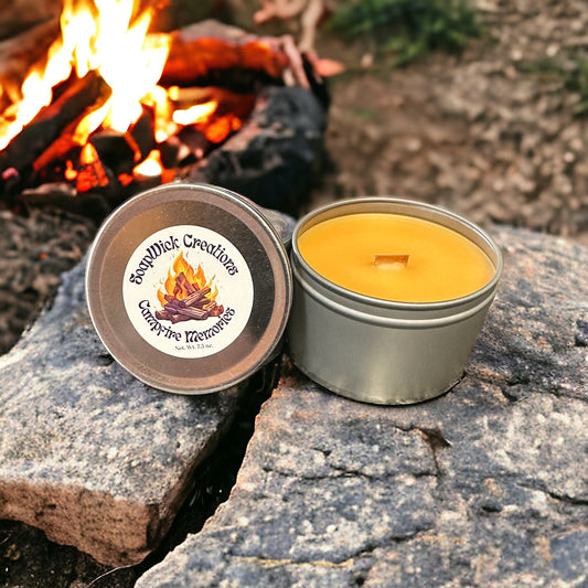 Orange candle in a silver metal candle tin sitting on a rock with a campfire in the background. The scent smells like a campfire burning.