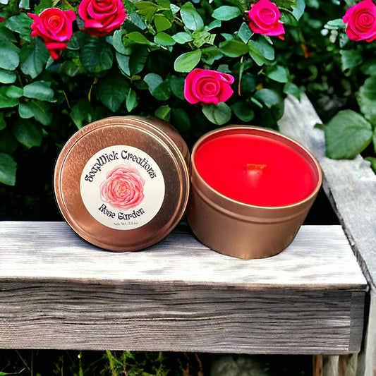 Rose scented candles in a rose colored tin on a rustic bench with rosebush in the background.