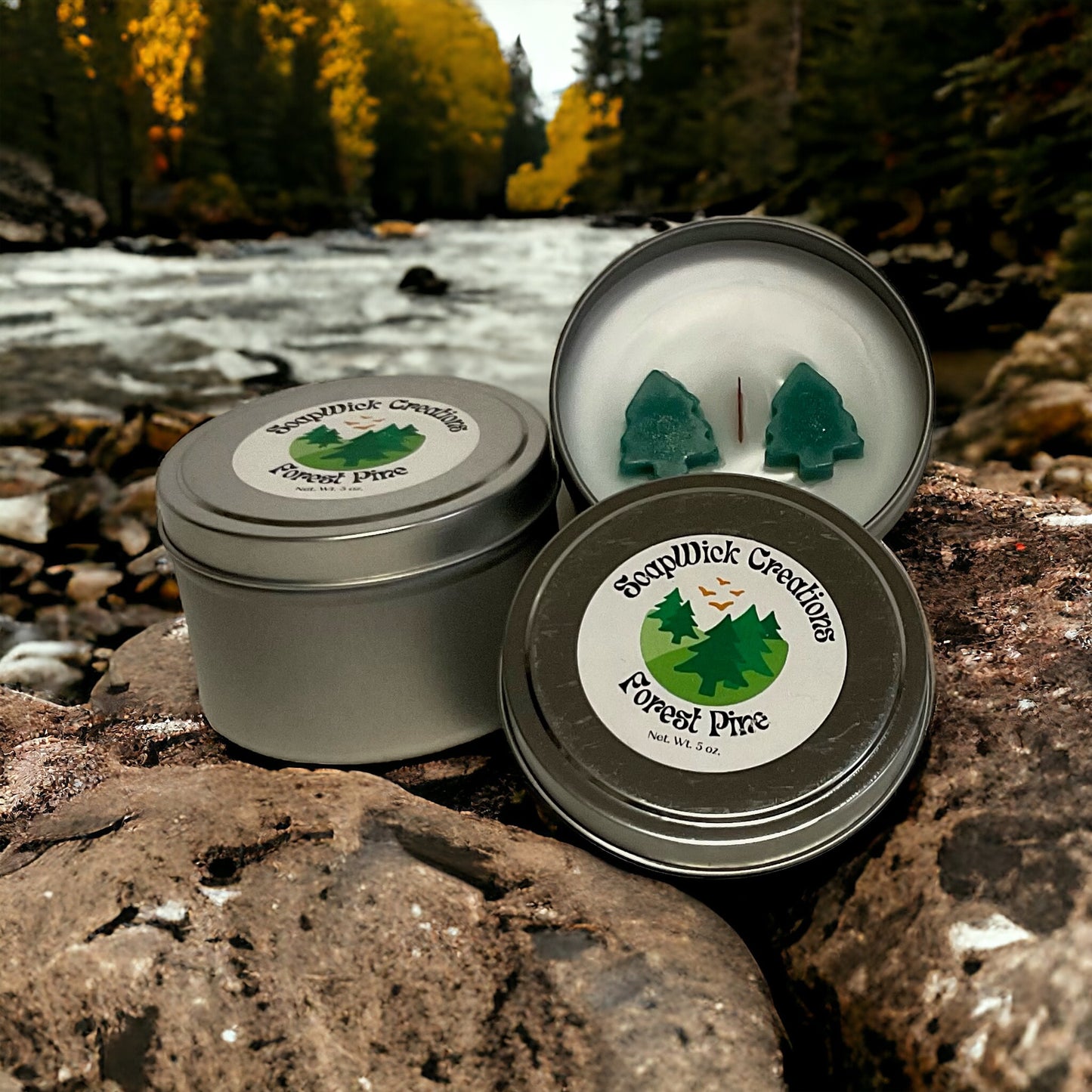 White Forest Pine scented candle in a Silver metal tin sitting on a rock with a river and pine forest in the background.