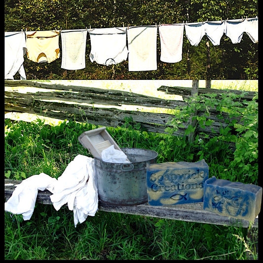 Photo of linen day, scented soap sitting on a bench with a wash, bucket and laundry with clothes hanging on a clothesline in the background.