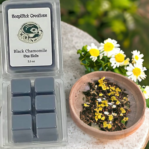 Gray colored black chamomile tea scented wax melt sitting on a stone with chamomile flowers and tea in a bowl sitting next to it.