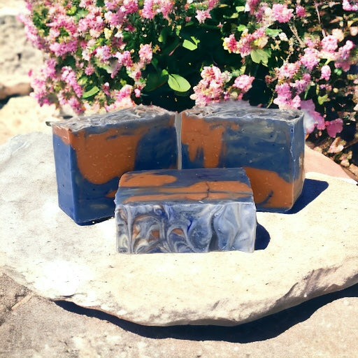 Photo of red and blue hippie chick soap Sitting on a stone surface with patchouly plant flowering in the background.