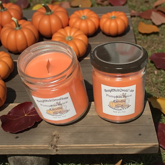 Two orange pumpkin spice candles on a wooden surface with pumpkins in the background.