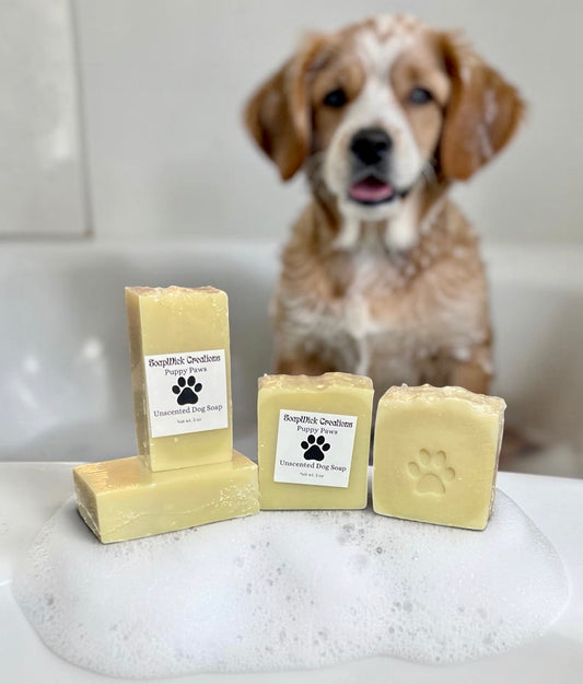 Picture of a dog with lather on its fur sitting in a bath with the four bars of puppy paws, unscented dog soap in front of him.