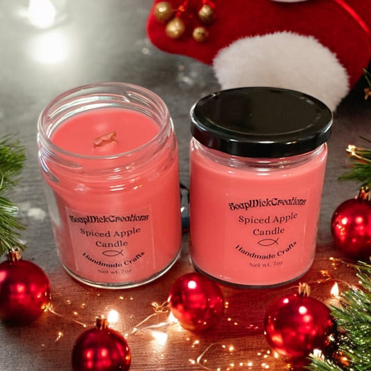 Two Reddish colored candles with spiced apple scent on a table with Christmas ornaments and a stocking in the background.