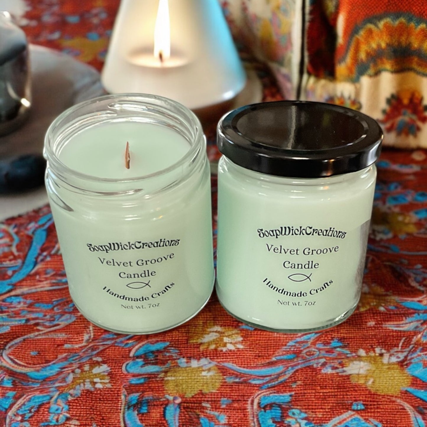 Two light green candle jars, sitting on a colorful tablecloth with a lava lamp in the background.