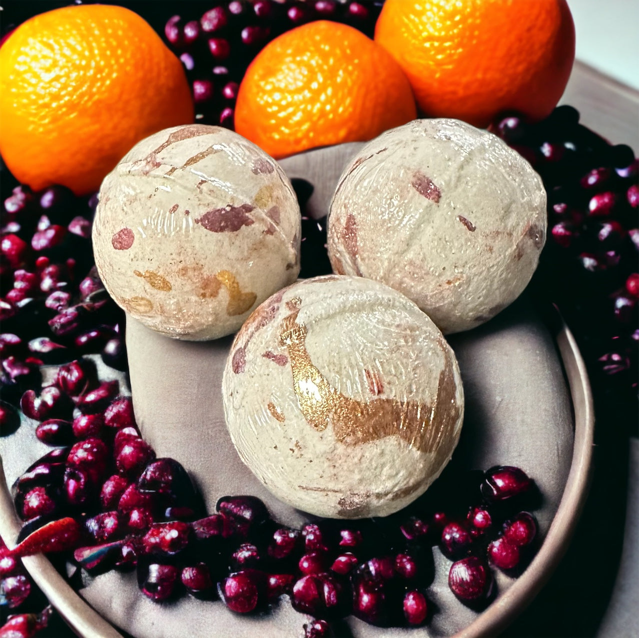 Three orange cranberry bath bombs in a bowl of cranberries with oranges in the background