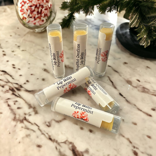 Photograph of six Peppermint flavored  lip balm tubes with a Christmas tree and a jar of peppermint candies in the background.