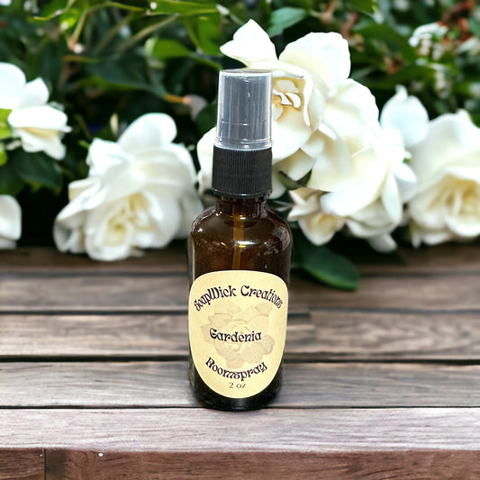 Photograph of a 2 ounce spray bottle with gardenia scent, sitting on a wooden bench with gardenia bush and gardenias in the background.