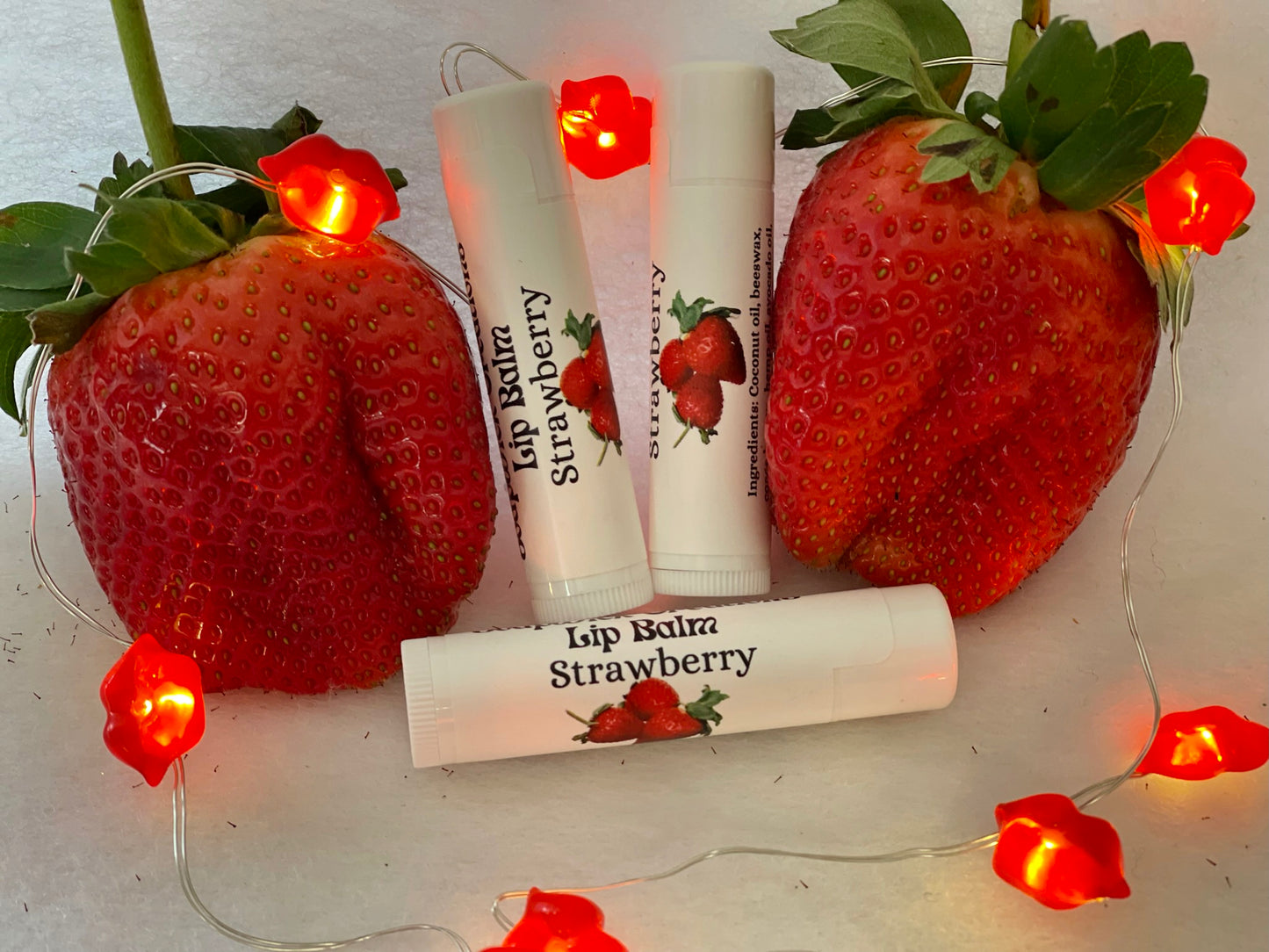 Tubes of strawberry lip balm between two strawberries with lit lips around it