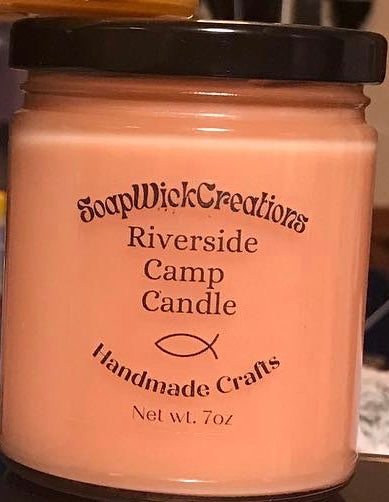 Photo of a light orange candle with the scent of campfire, coconut, and  oakmoss  and cedar scent 