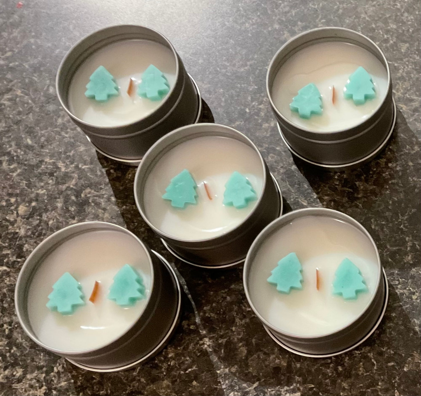 Photograph of Silver tins containing white candles with pine scent and green pine tree embeds