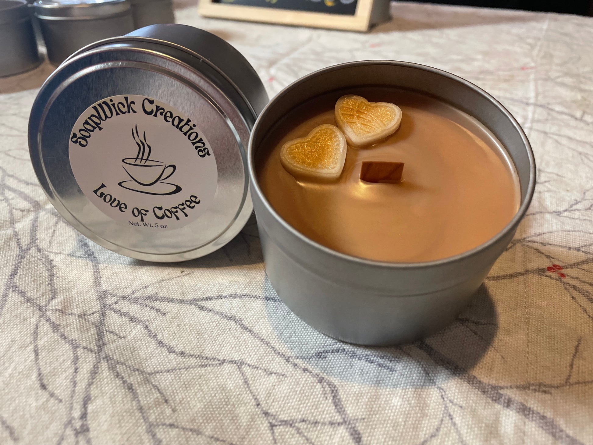 Photo of a light brown candle with heart, embeds and coffee scent in a silver tin
